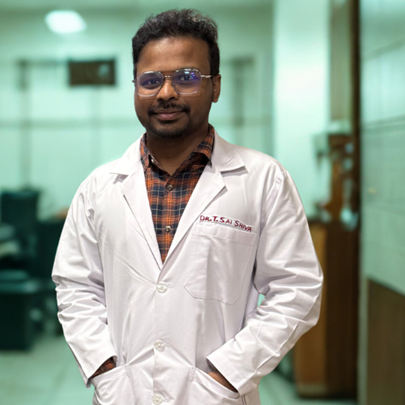 Male doctor in a white lab coat standing in a tidy clinic hallway, hands in pockets and smiling.