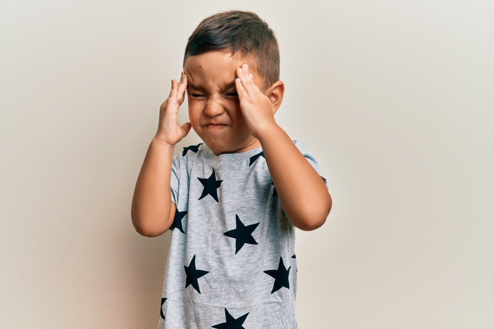 Young boy with a star-patterned shirt presses his temples, showing frustration or a headache.